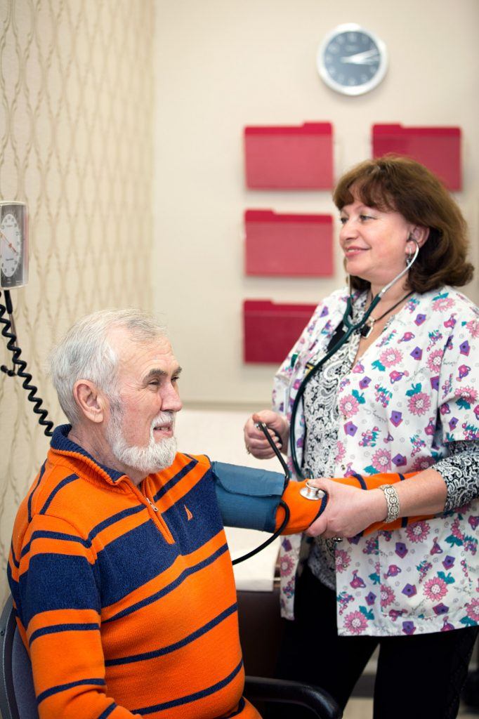 Nurse checking blood pressure of a patient suffering from arthritis headache.