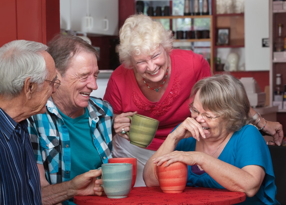 Four happy senior people having chat while holding mugs.