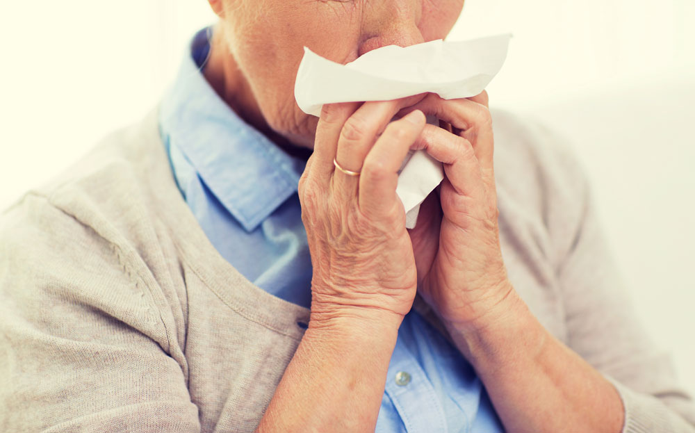Sick senior woman suffering from cold and flu blowing nose to paper napkin