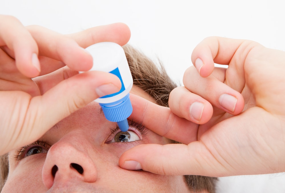 Man putting eye drops in his eyes to stop vision from worsening