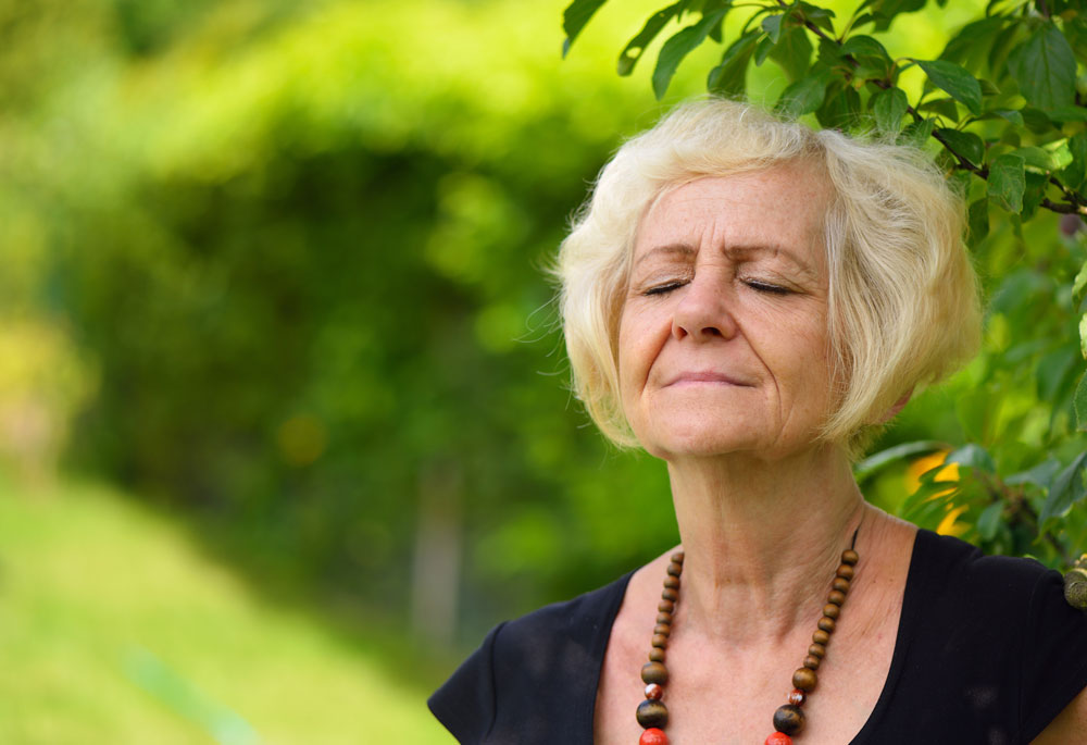Elderly woman doing breathing yoga in natural environment to keep calm to heal overactive nerves.