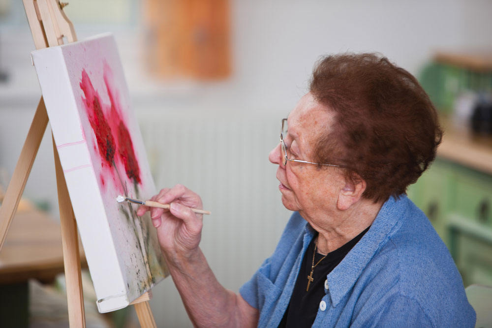 Senior woman painting on canvas as part of rehab activities