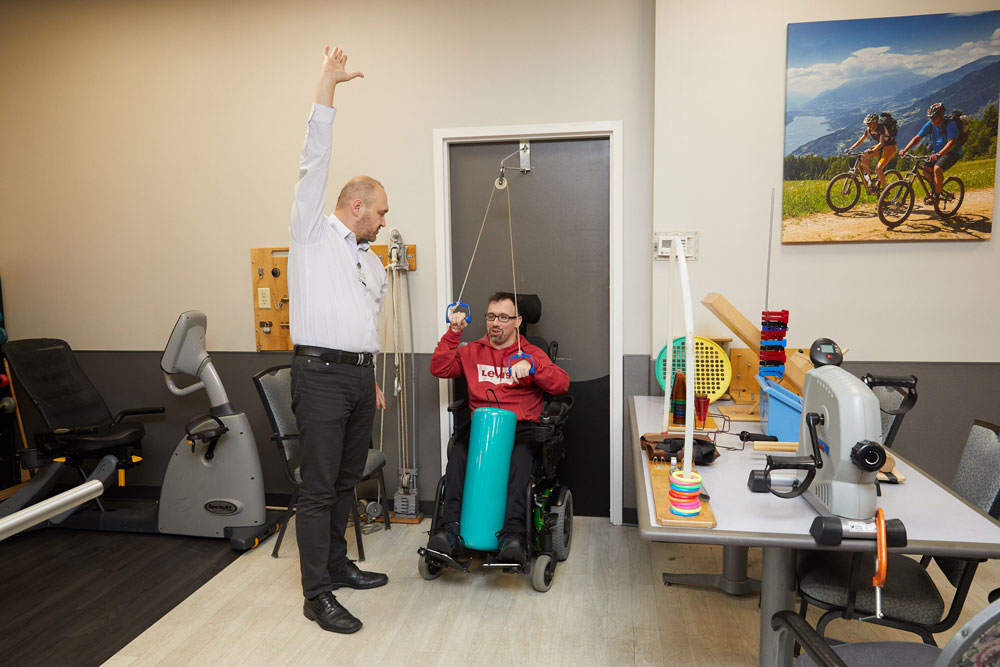 Physical therapist helping man suffering from neurological disorders with physical therapy