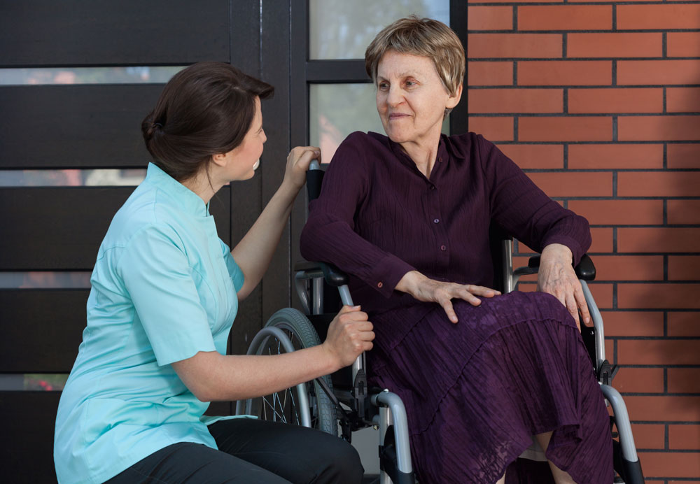 Nurse talking with an elderly woman with poor mobility in joints sitting on a wheelchair
