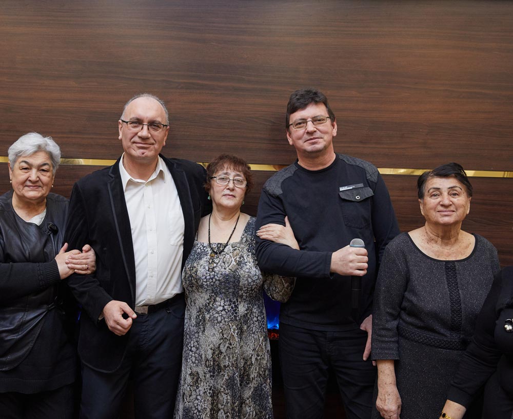 Five senior people standing against a wooden wall holding each other hands in an elderly day care