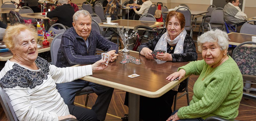 Four elderly people sitting and playing cards to prevent chronic diseases by eliminating risk factors.