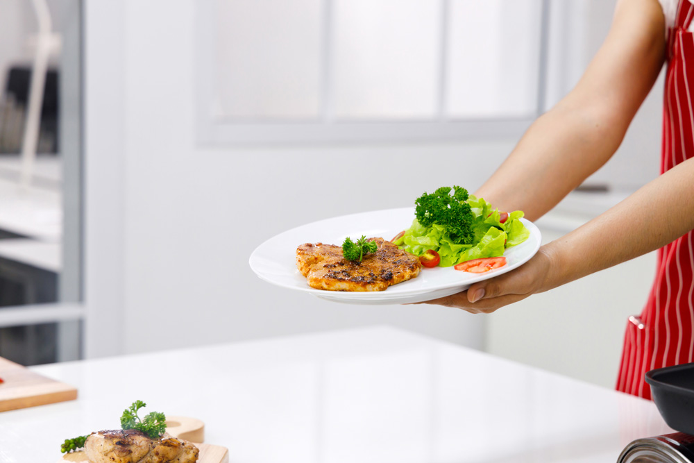 Woman chef holding dish of pork steak and salad. Eat healthy food to avoid faster heartbeat after eating.