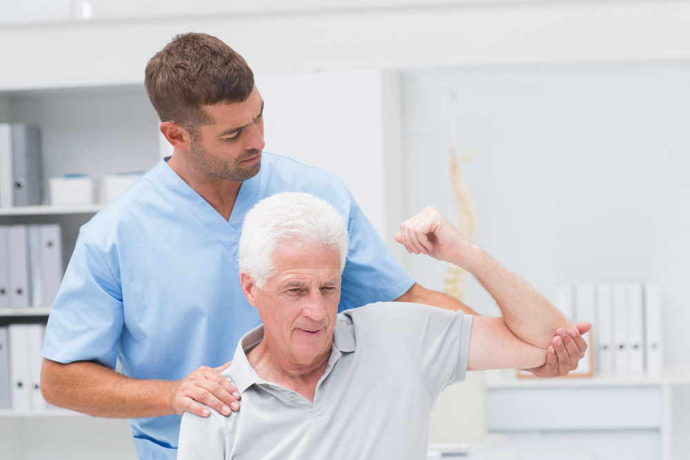 Therapist helping senior man with broken shoulder.
