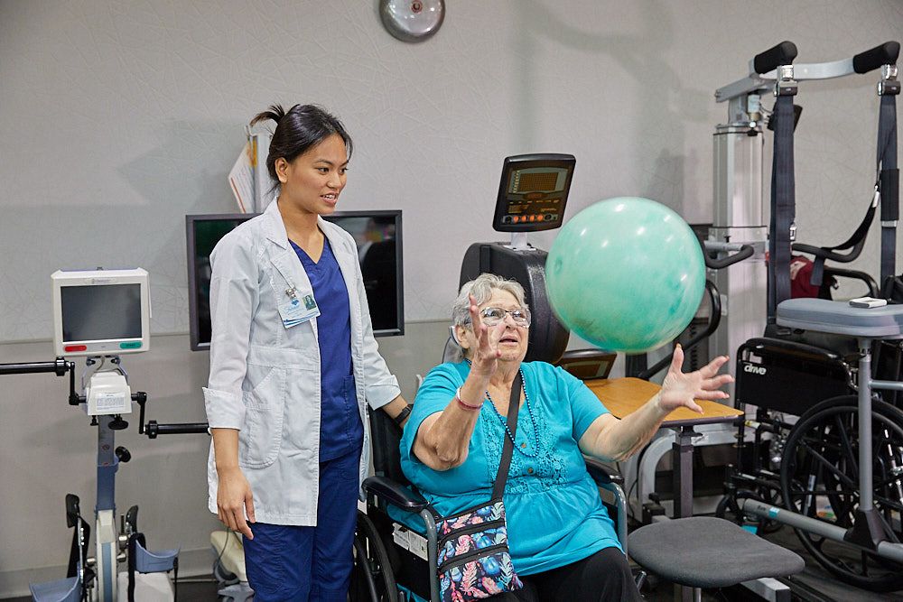 Therapist and elderly woman playing with yoga ball to prevent fatigue after exercise.