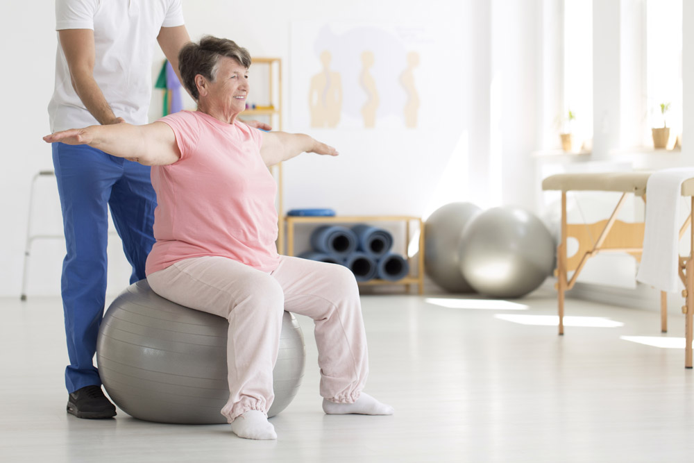 Nurse helping elderly woman to increase range of motion with balance exercises on a fit ball